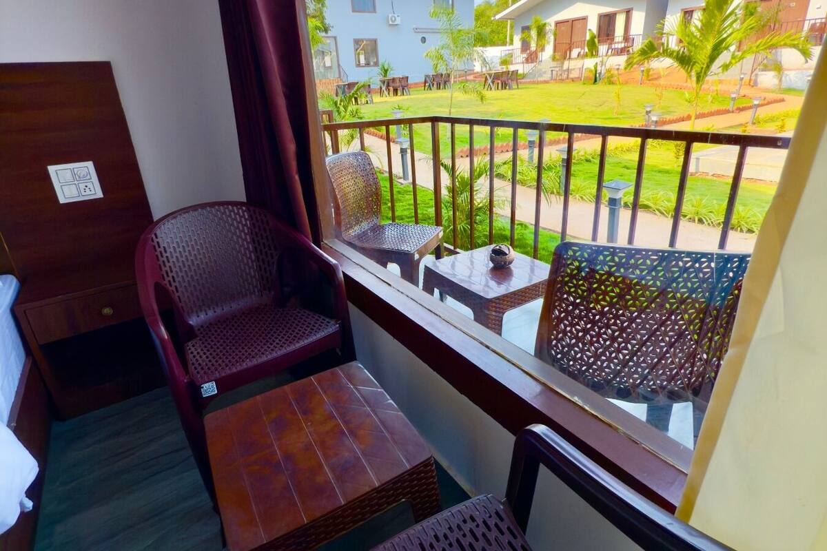 A balcony with a view of a well-maintained lawn and buildings. There are two wicker chairs and a small table.