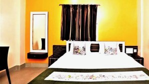 A bedroom with a large bed, a bedside table, a mirror, and a window with curtains. - DhamStay Hotel Krishna Residency Puri (Puri)