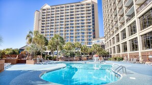 Un hôtel doté d’une grande piscine, de palmiers et, en arrière-plan, d’un immeuble de grande hauteur.