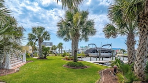 A well-maintained lawn with palm trees, a dock with boats, and a pathway leading to a building.