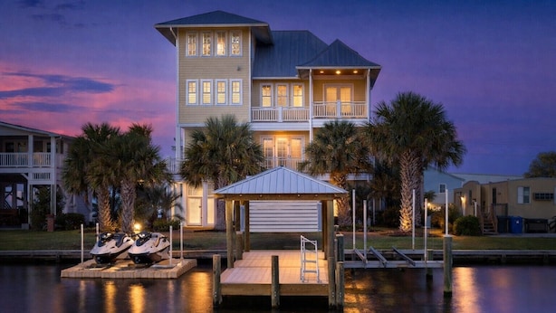 A two-story house with a dock, a covered area, and a boat.