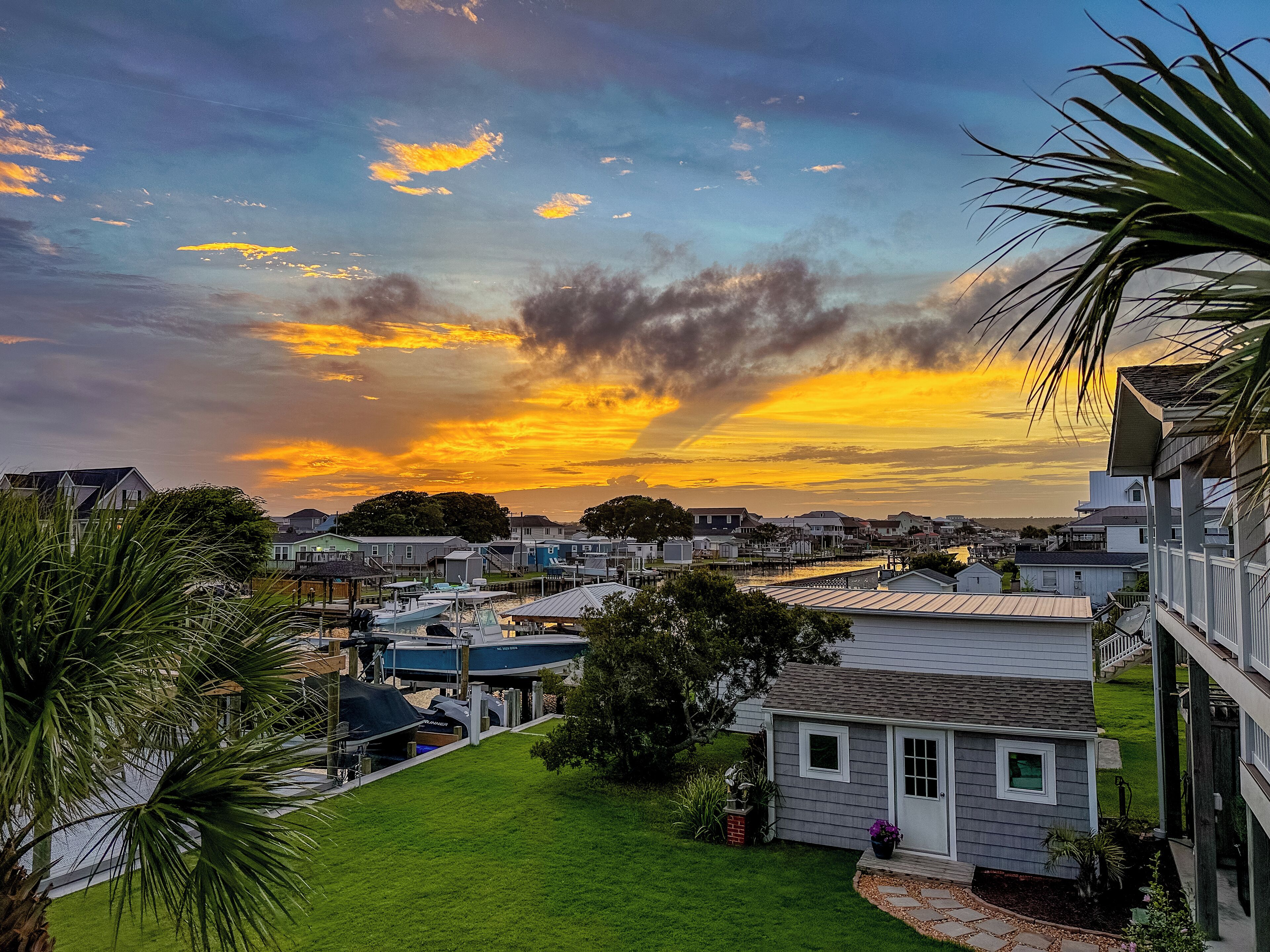 A residential area with houses, a grassy yard, and boats docked near a waterfront.