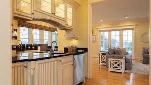 A spacious kitchen with white cabinetry and a black countertop, a dining area with a white table and chairs, and a living room with a gray sofa and a coffee table.