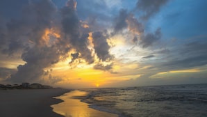 A beach with a sunset, clouds, and a calm sea.