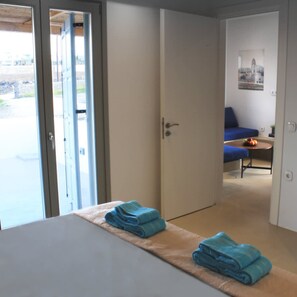 Et hotelværelse med en seng, en dør der fører ud til en balkon, og en blå sofa i det tilstødende rum.