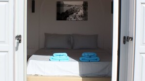 Un dormitorio con cama, almohadas, una toalla doblada y un cuadro en la pared.