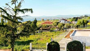 A landscaped garden with a paved pathway, two large bushes, and a view of houses and mountains in the distance. - Chalkidiki Sea Aura - Eva s Cozy Getaway (Nea Propontida)