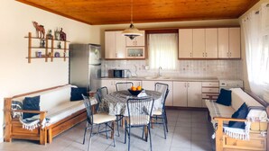 A cozy kitchen with wooden ceiling, a dining table with chairs, a refrigerator, a microwave, and a sink. - Chalkidiki Sea Aura - Eva s Cozy Getaway (Nea Propontida)