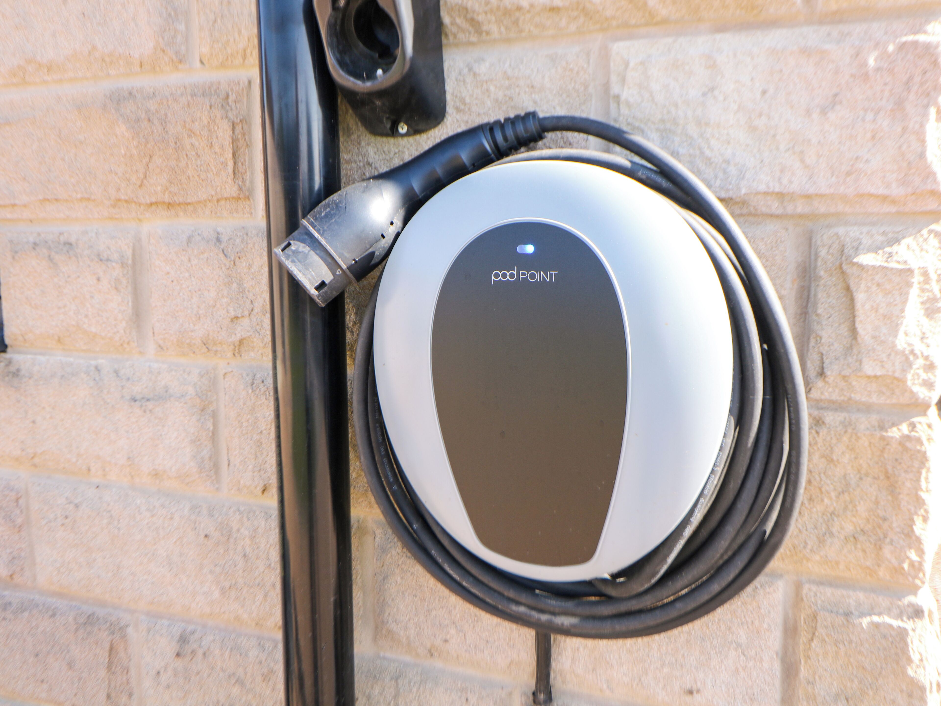 A pod point charging station mounted on a brick wall.