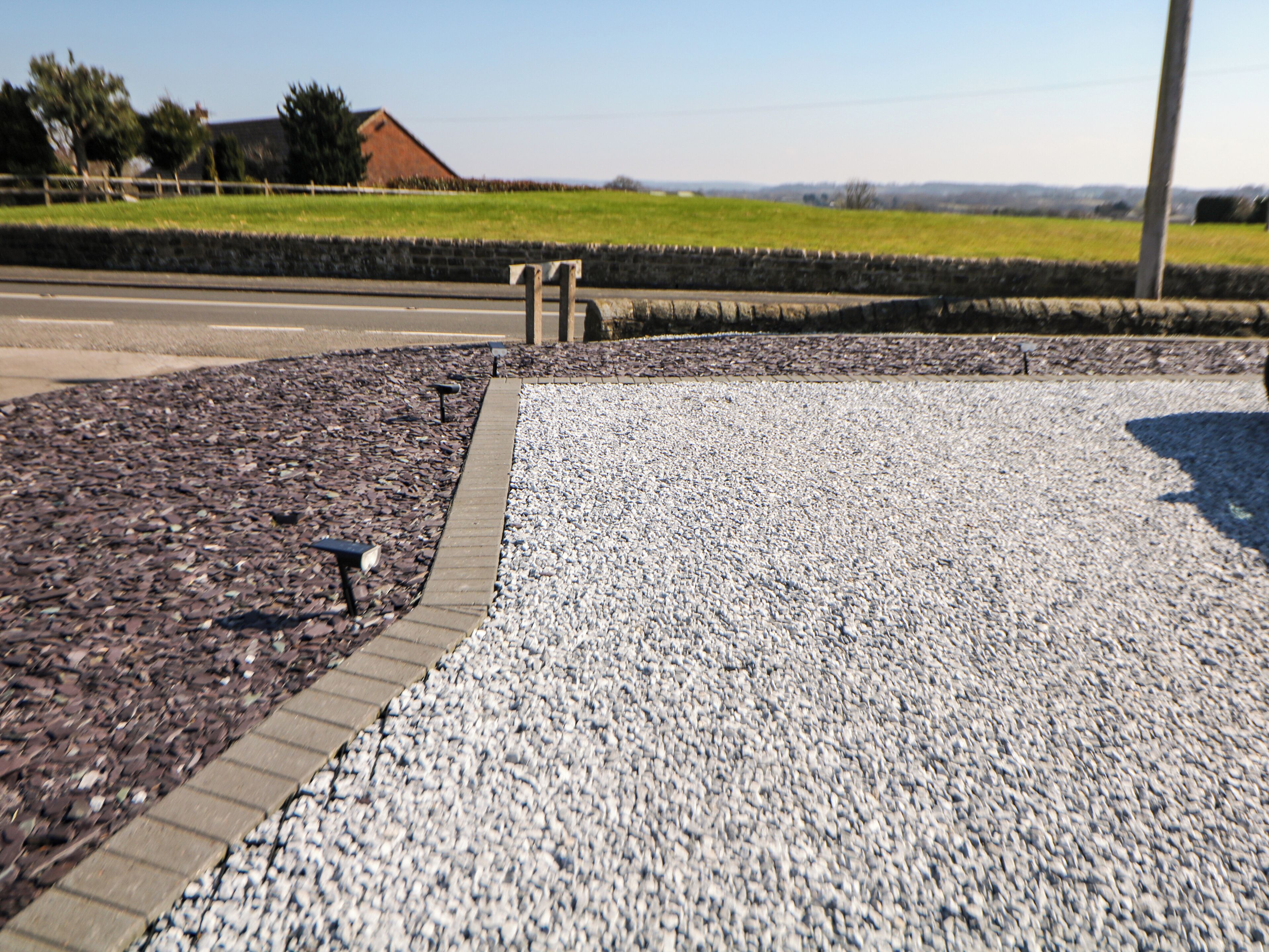 A gravel pathway with a brick border, leading to a grassy field.