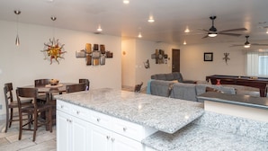 Eine geräumige Küche mit Granit Arbeitsplatten, ein Essbereich mit Holzsesseln und ein Wohnbereich mit grauem Sofa.