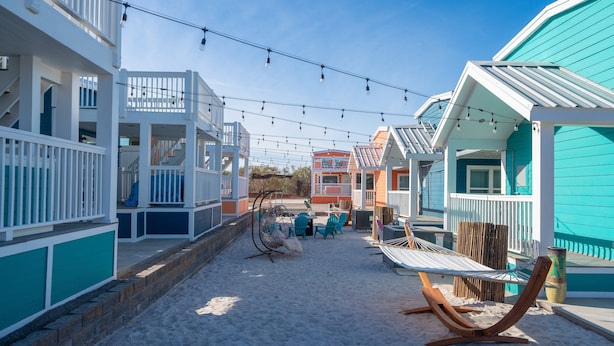 Un bien immobilier situé en bord de mer, composé de plusieurs bâtiments aux couleurs vives, doté d’un espace extérieur aménagé et illuminé de guirlandes lumineuses.