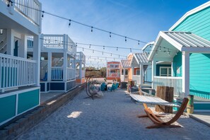 A beachfront property with multiple colorful buildings, outdoor seating, and string lights. - Guitars & Tiki Bars, Roadrunner Resort (Parker)