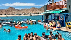 Une zone avec une piscine où des personnes se baignent, un poste de surveillance pour les sauveteurs, et une vue sur la plage en arrière-plan.