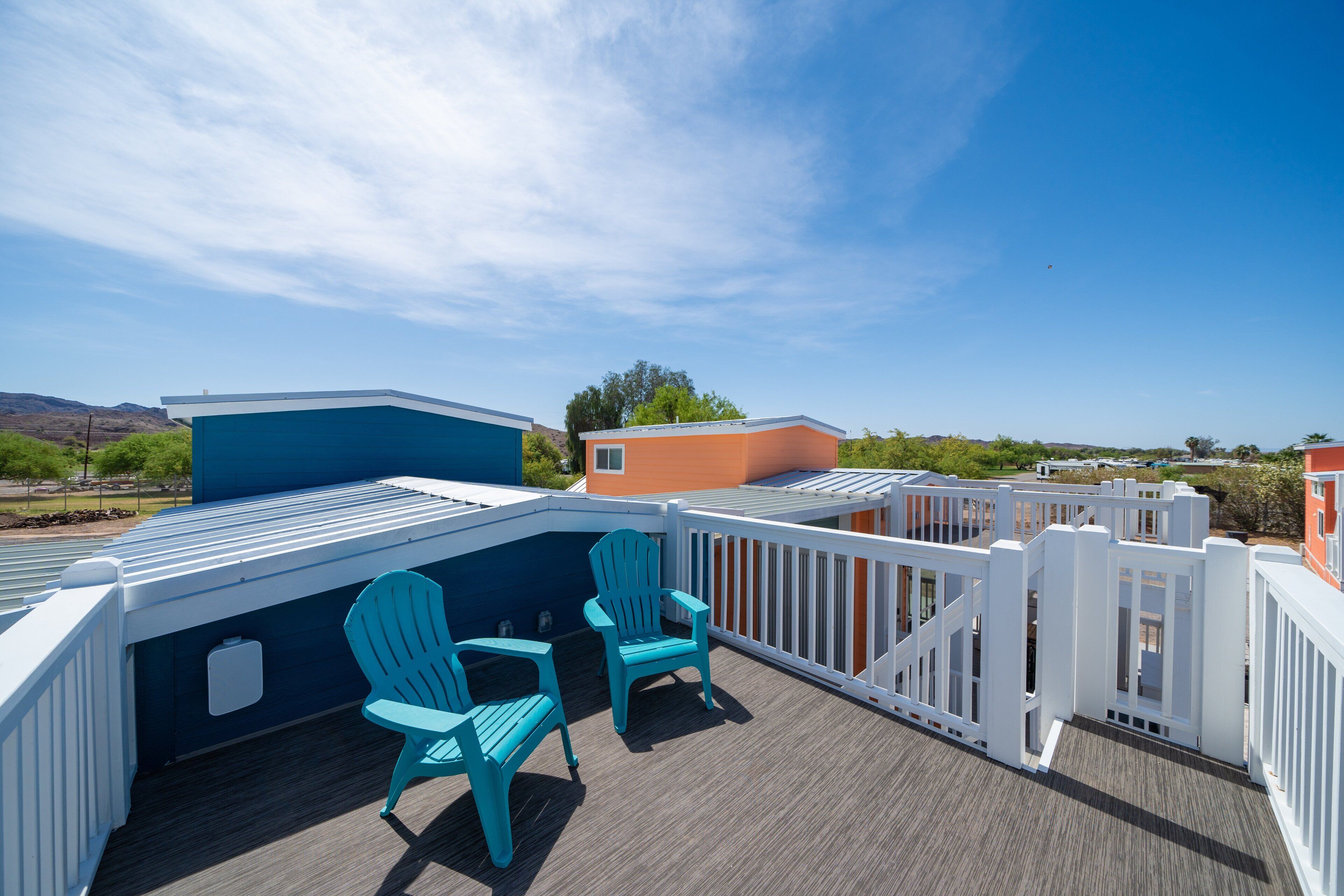 A deck with two chairs and a railing, overlooking a residential area with houses and a clear sky.