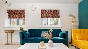 A living room with a teal sofa, a yellow sofa, a white coffee table, and a clock on the wall. - Spacious 4bd 3.5bt - Etihad COOP -Cinema PoolTable (Greater Manchester)