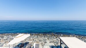 A rocky shoreline with clear blue sea and a white structure with a roof. - Pool, Mountain & Sea View 6BR Villa w/ Asst & Driver Room,Heated Pool,BBQ Area (Fujairah)