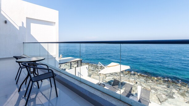 A balcony with a view of the sea, featuring a table and chairs, and a small seating area with an umbrella. - Pool, Mountain & Sea View 6BR Villa w/ Asst & Driver Room,Heated Pool,BBQ Area (Fujairah)