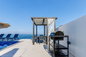 A rooftop pool area with lounge chairs, a grill, and a view of the ocean. - Pool, Mountain & Sea View 6BR Villa w/ Asst & Driver Room,Heated Pool,BBQ Area (Fujairah)