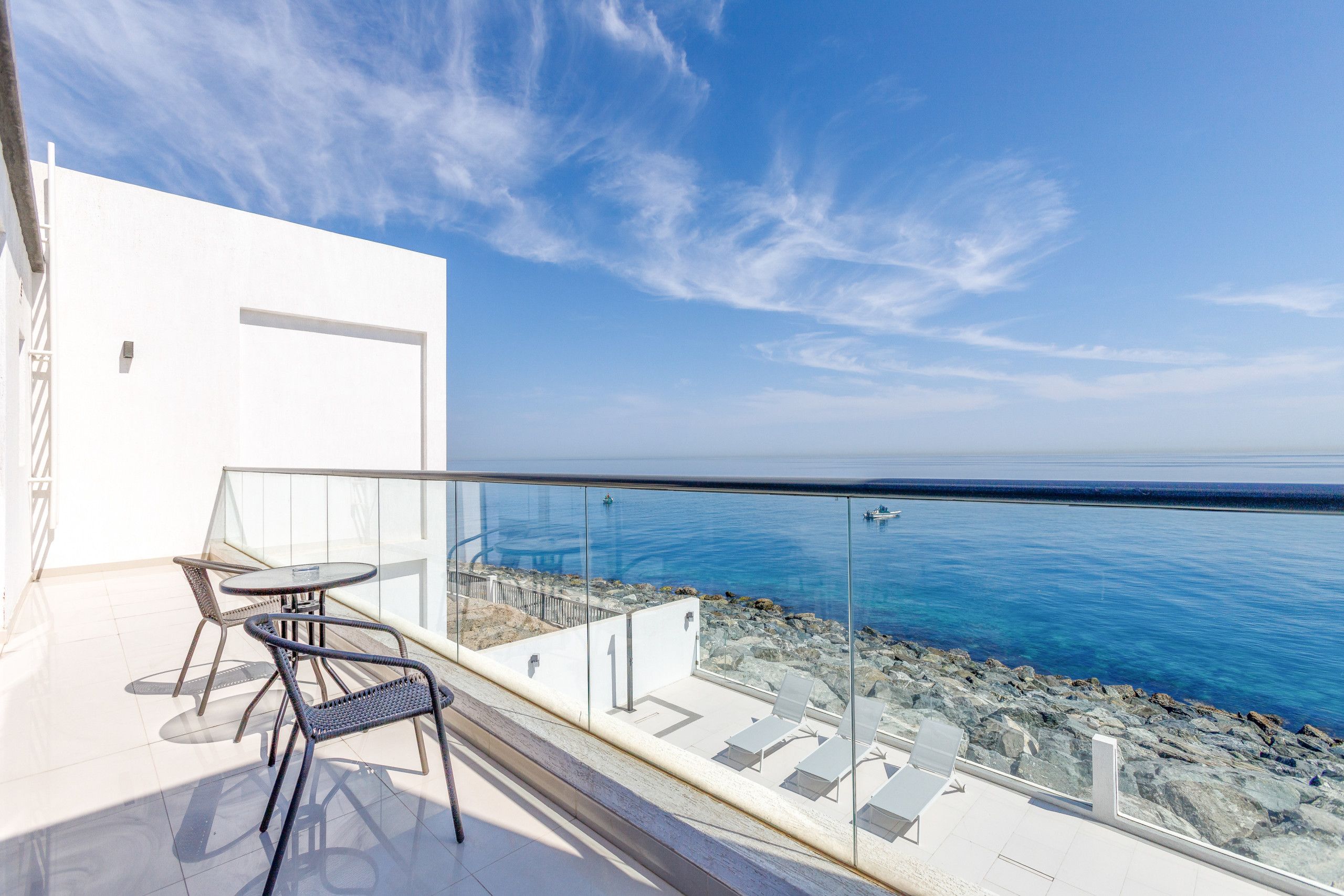 A balcony with a glass railing overlooking a rocky coastline and the sea.