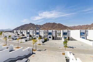 A modern urban street with white buildings, a clear sky, and distant mountains.