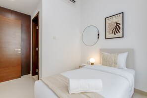 A hotel room with a large bed, a bedside table with a lamp, a round mirror, and a framed artwork on the wall.