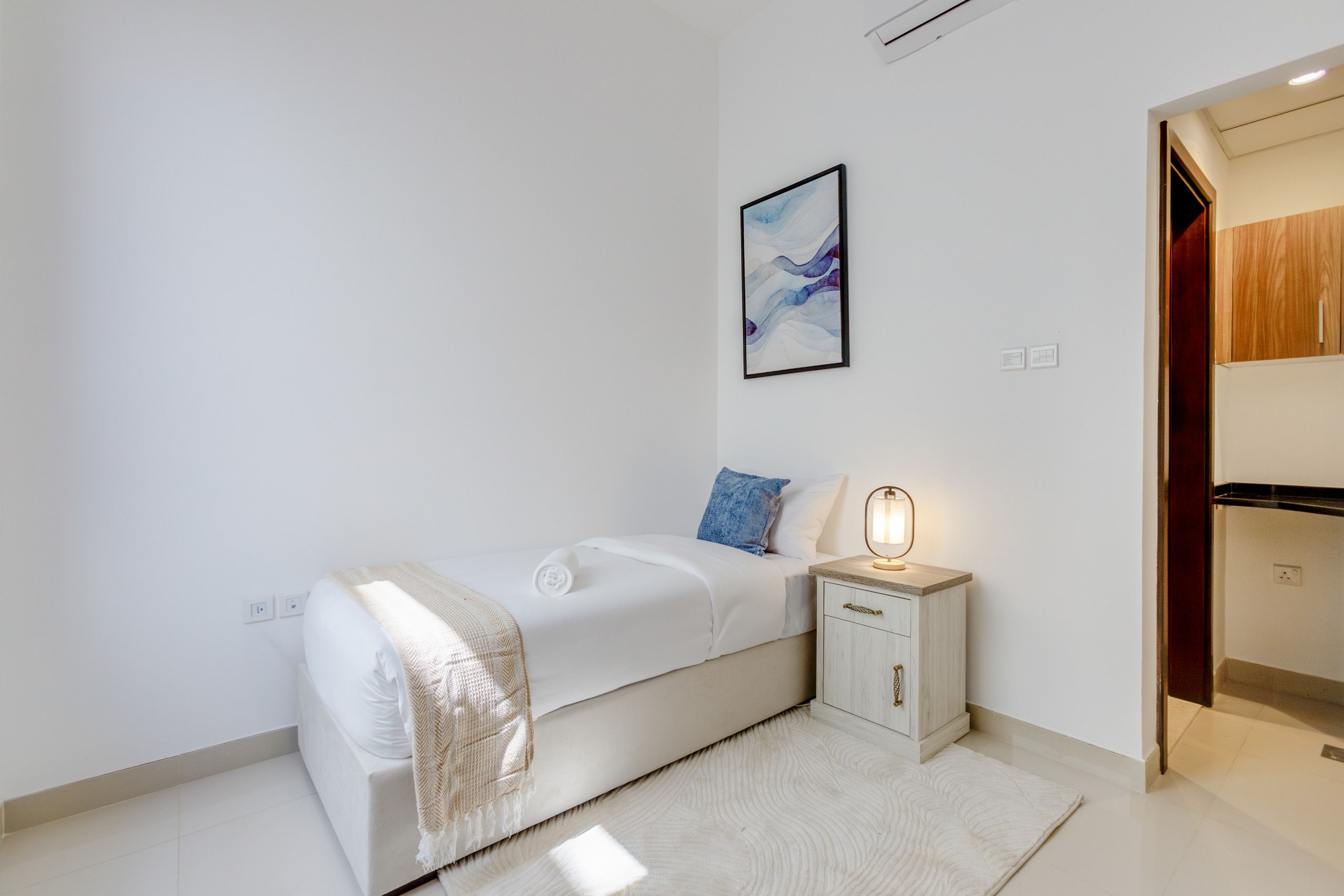 Une chambre à coucher moderne avec un lit simple, une table de chevet avec une lampe et un tableau abstrait encadré accroché au mur.