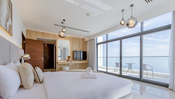 Una habitación de hotel moderna con una cama grande, un escritorio y una televisión. Cuenta con un balcón con vista al mar.