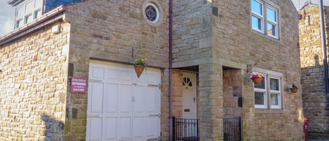 A stone building with a white garage door, a small entrance with a door, and a window with a flower basket.