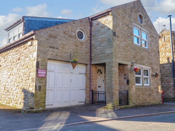 A stone building with a white garage door, a small entrance with a door, and a window with a flower basket. - Vive House (Preston)