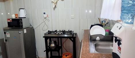 A compact kitchen with a refrigerator, microwave, gas stove, sink, and a water dispenser.