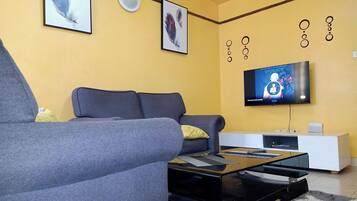 Un salon moderne avec un canapé gris, une table basse noire et un téléviseur à écran plat fixé au mur.