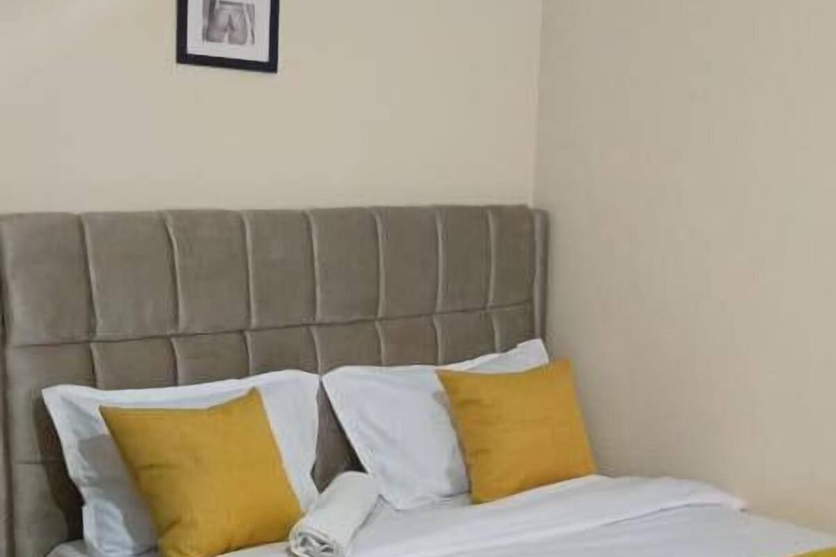 Uma cama bem arrumada com roupa de cama branca e amarela, uma cabeceira e uma mesinha de cabeceira.