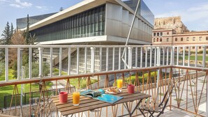 A balcony with a table set for breakfast, overlooking a modern building and a historic structure. - Acropolis Museum Retreat by GHH (Athina)