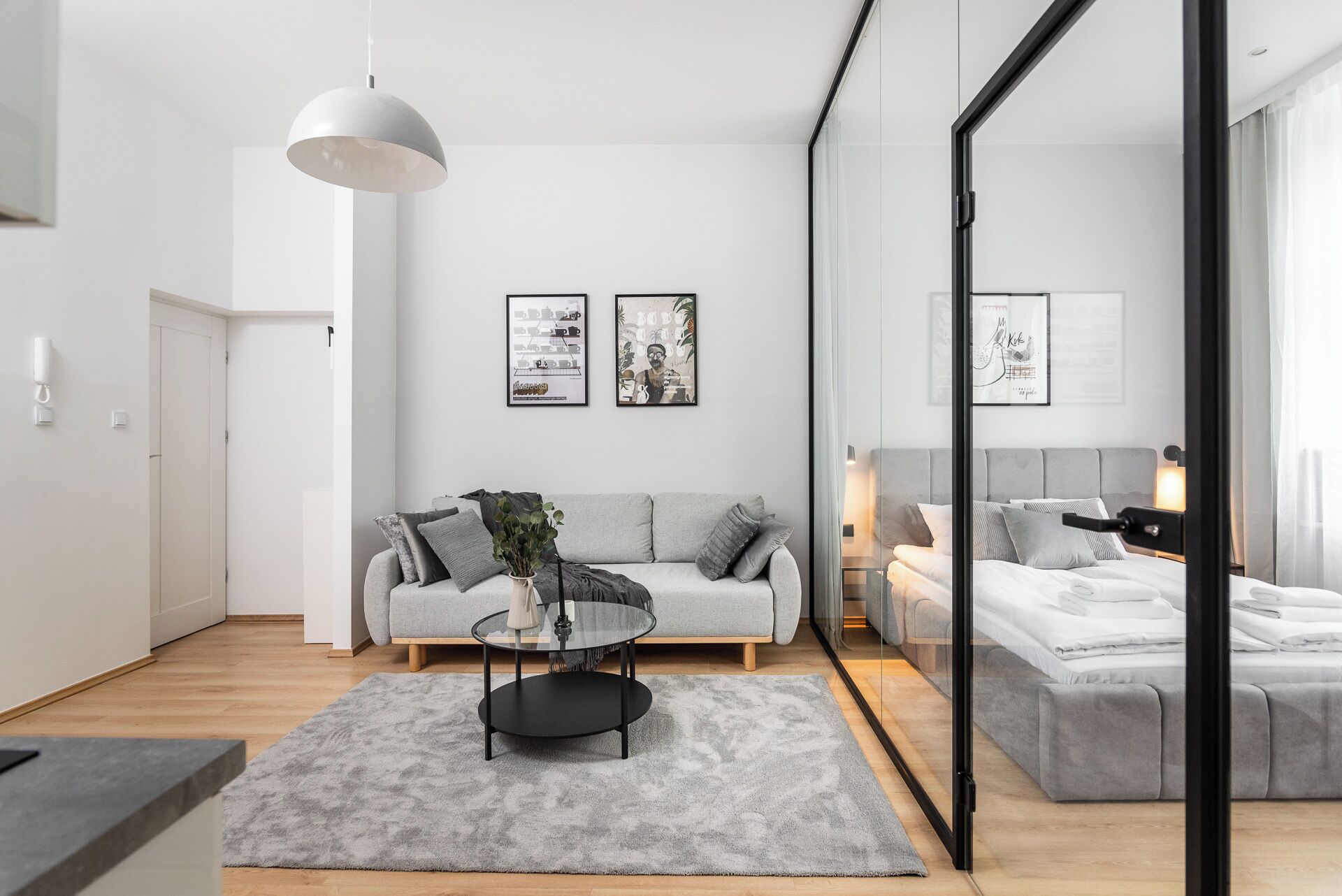 Un salon moderne avec un canapé gris, une table basse en verre et deux œuvres d’art encadrées accrochées au mur.
