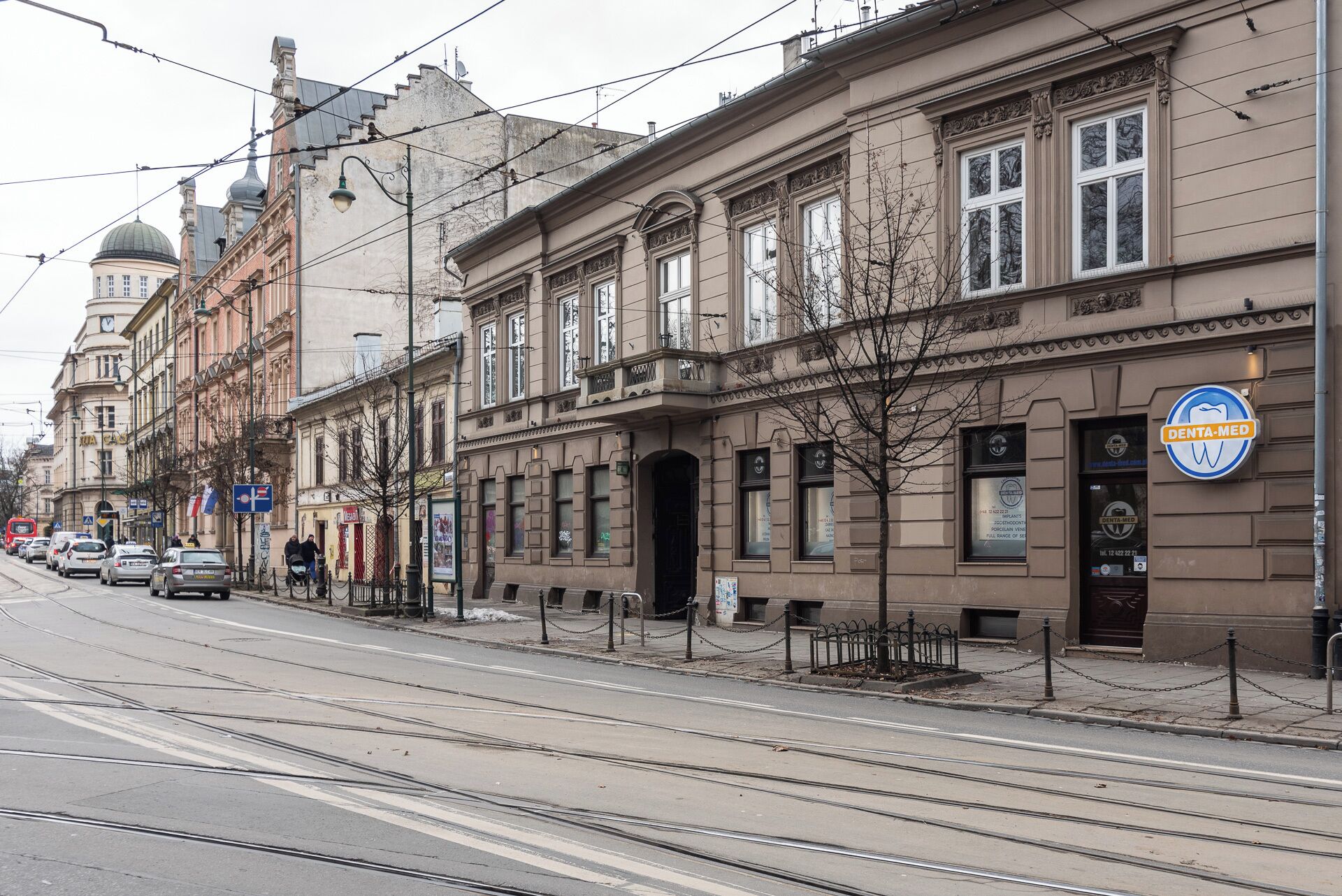 A street with tram tracks, historic buildings, and a dental clinic sign.