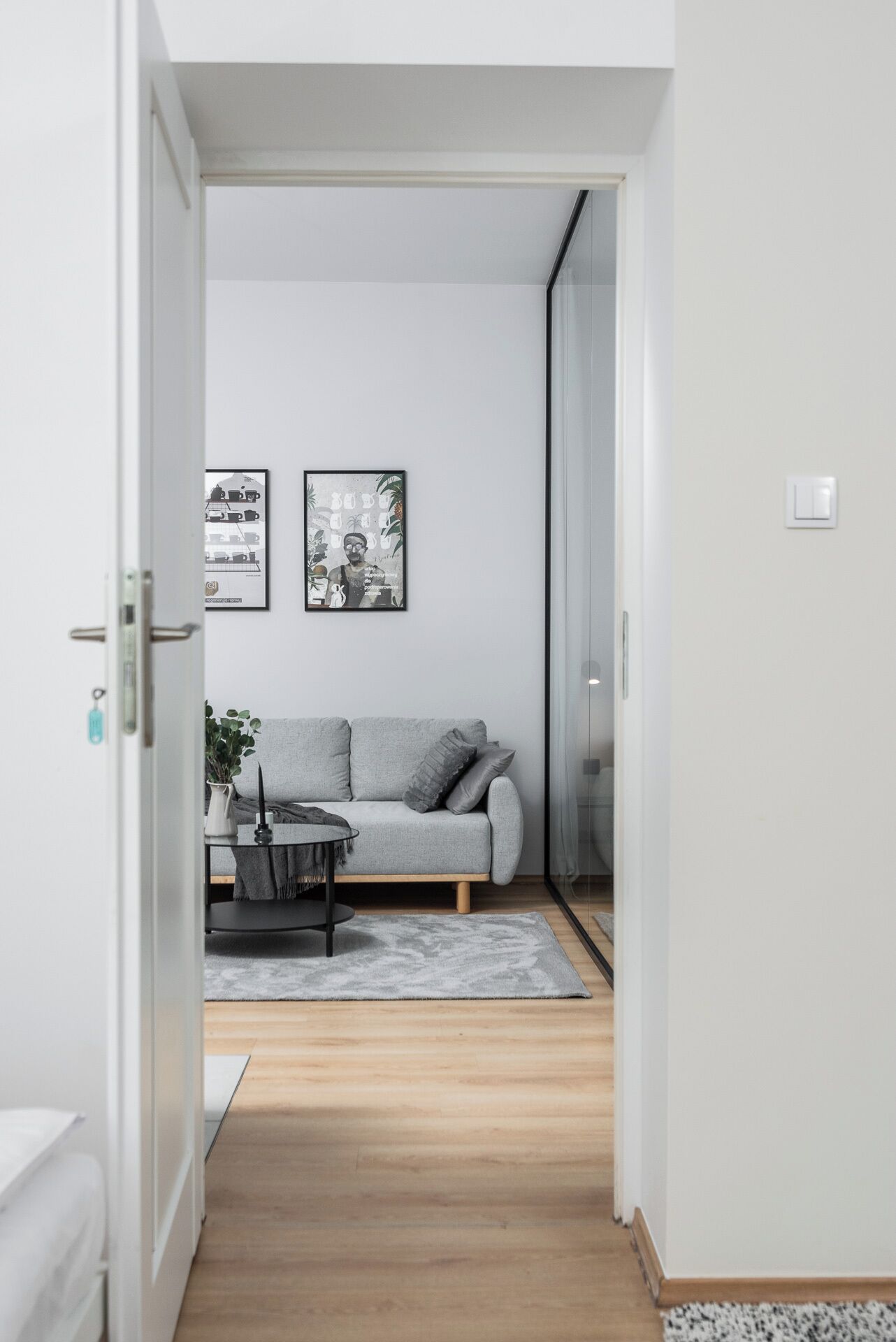 A minimalist living room with a grey sofa, a small table, and two framed pictures on the wall.