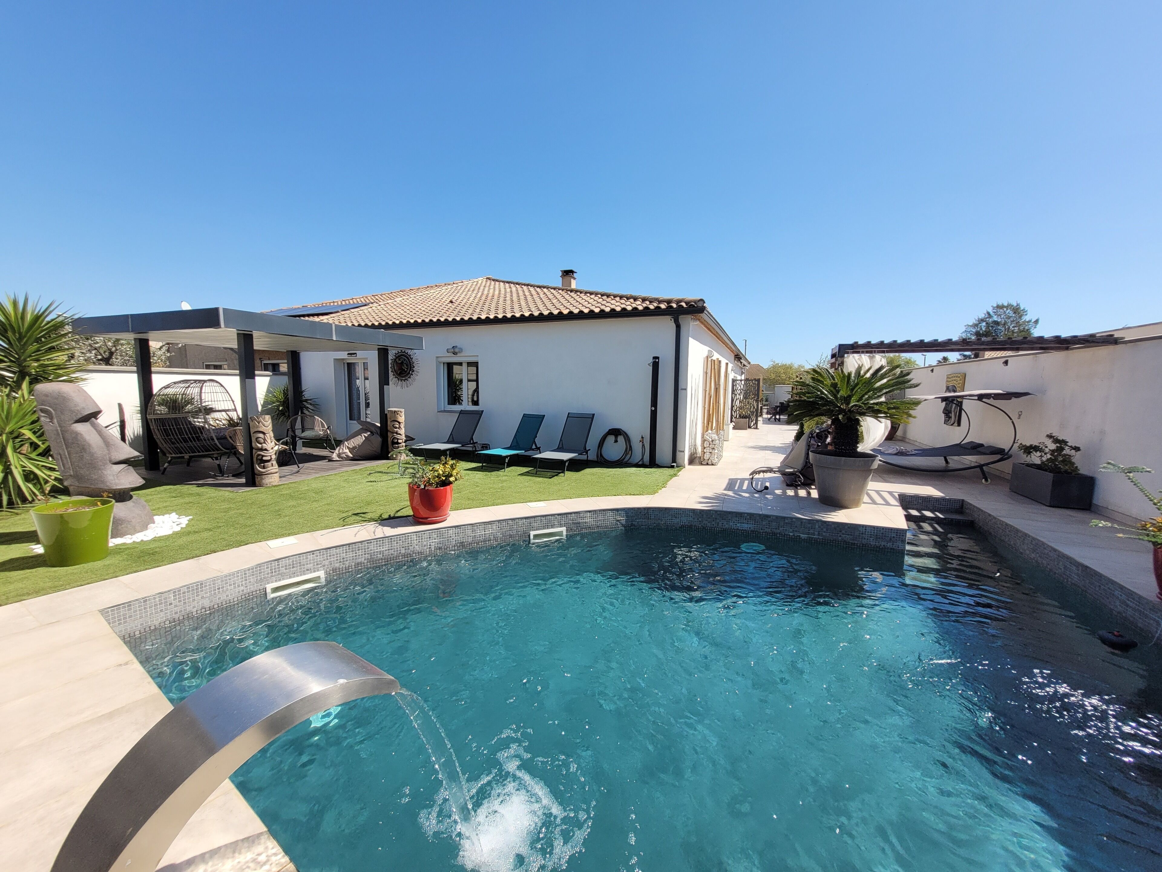 A swimming pool with a water fountain, surrounded by lounge chairs and a covered seating area.