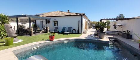 A swimming pool with a water fountain, surrounded by lounge chairs and a covered seating area.