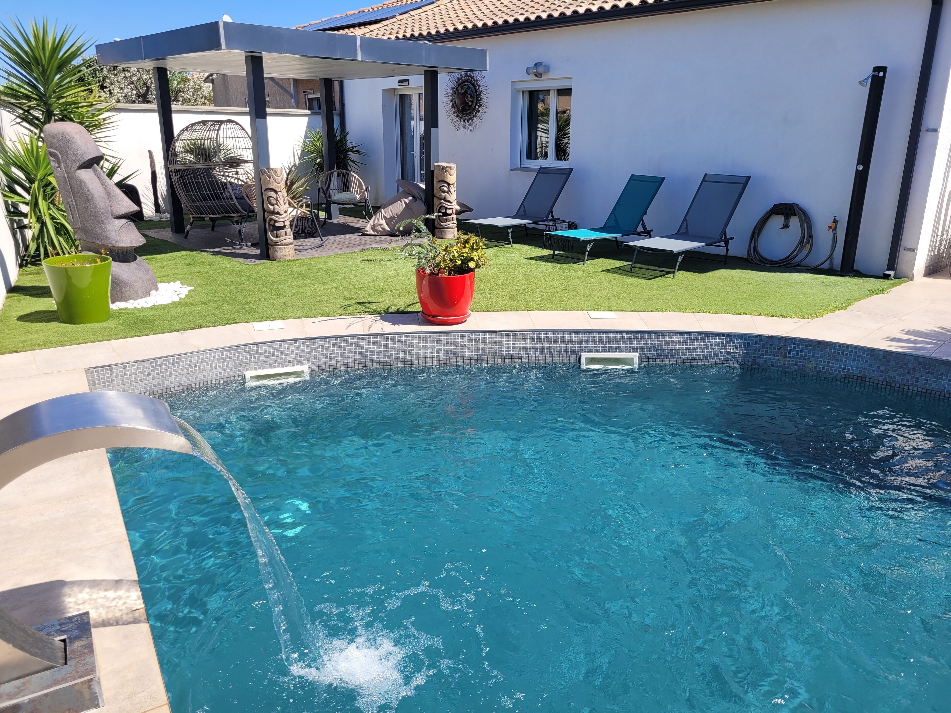 Una piscina con borde de azulejos, rodeada por un patio con sillas de descanso y una zona de estar cubierta.