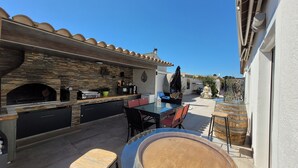 An outdoor patio with a stone fireplace, a glass table, and a seating area.