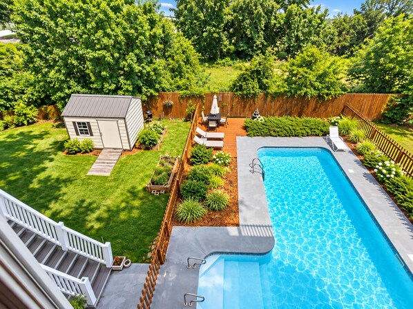 A backyard with a swimming pool, a small shed, and a wooden deck.