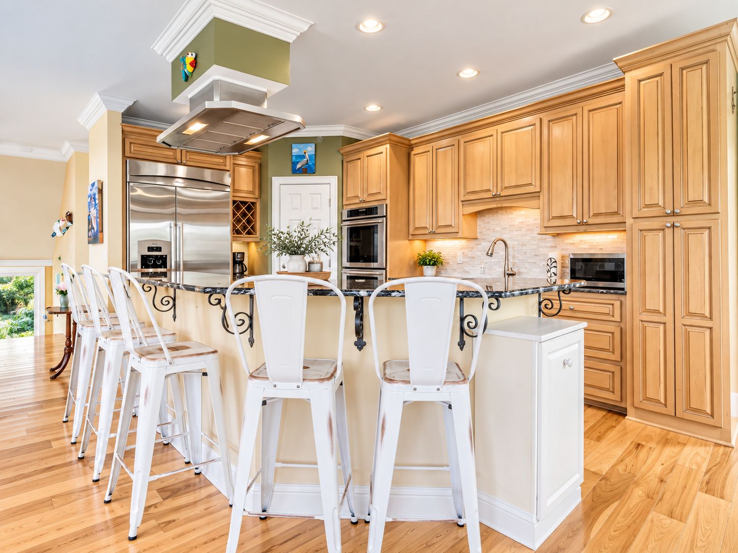 A modern kitchen with wooden cabinets, stainless steel appliances, and a bar area with white bar stools.