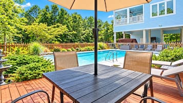 A wooden deck with a pool table, chairs, and an umbrella.
