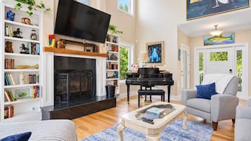 Una sala de estar con chimenea, televisor, piano y estantería.