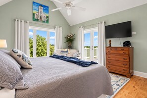 A bedroom with a bed, a dresser, a television, and a window with curtains.