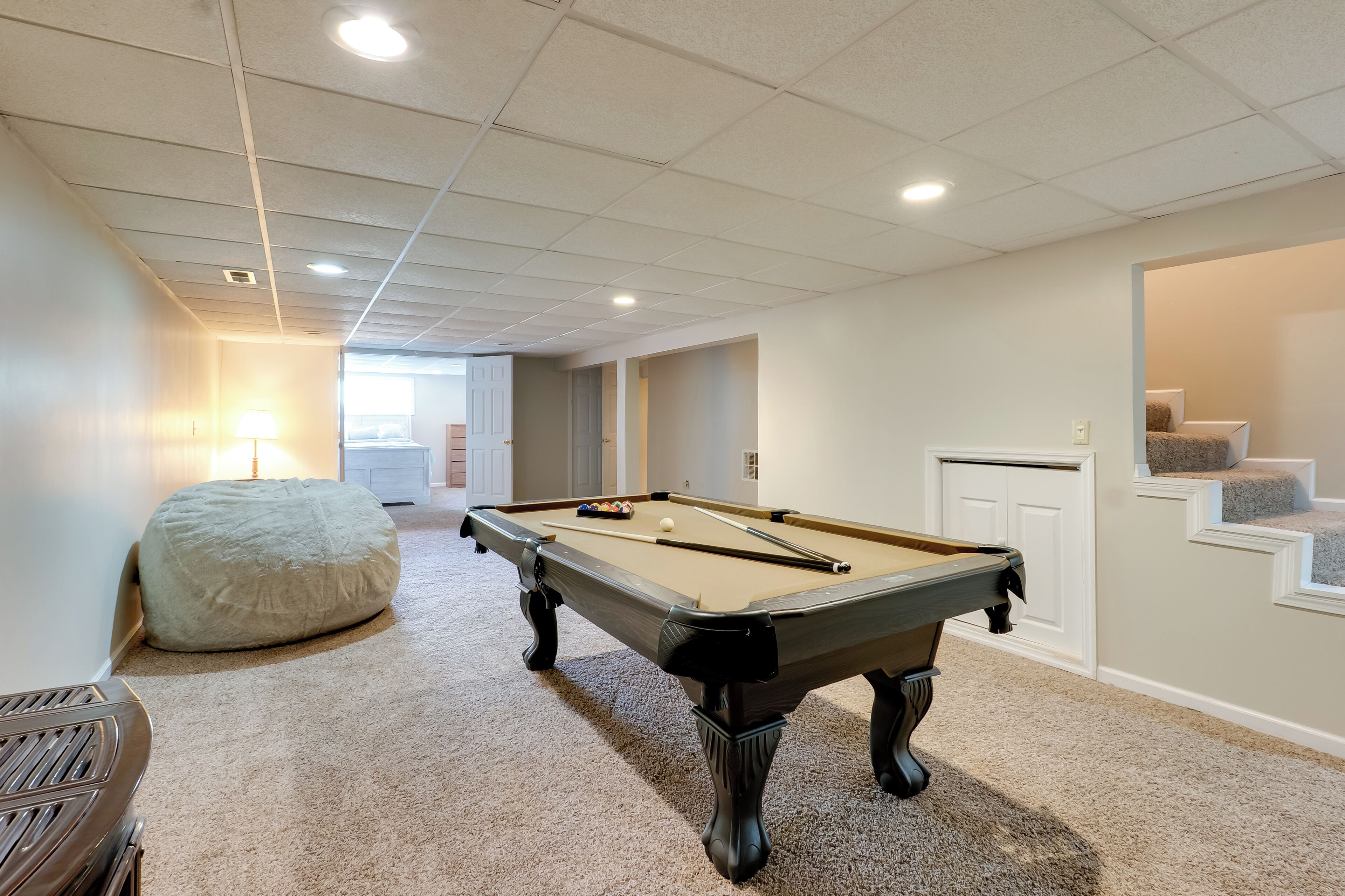 Une table de billard dans une pièce dont le sol est recouvert de moquette, avec un fauteuil en forme de sac et un escalier menant à un autre niveau.