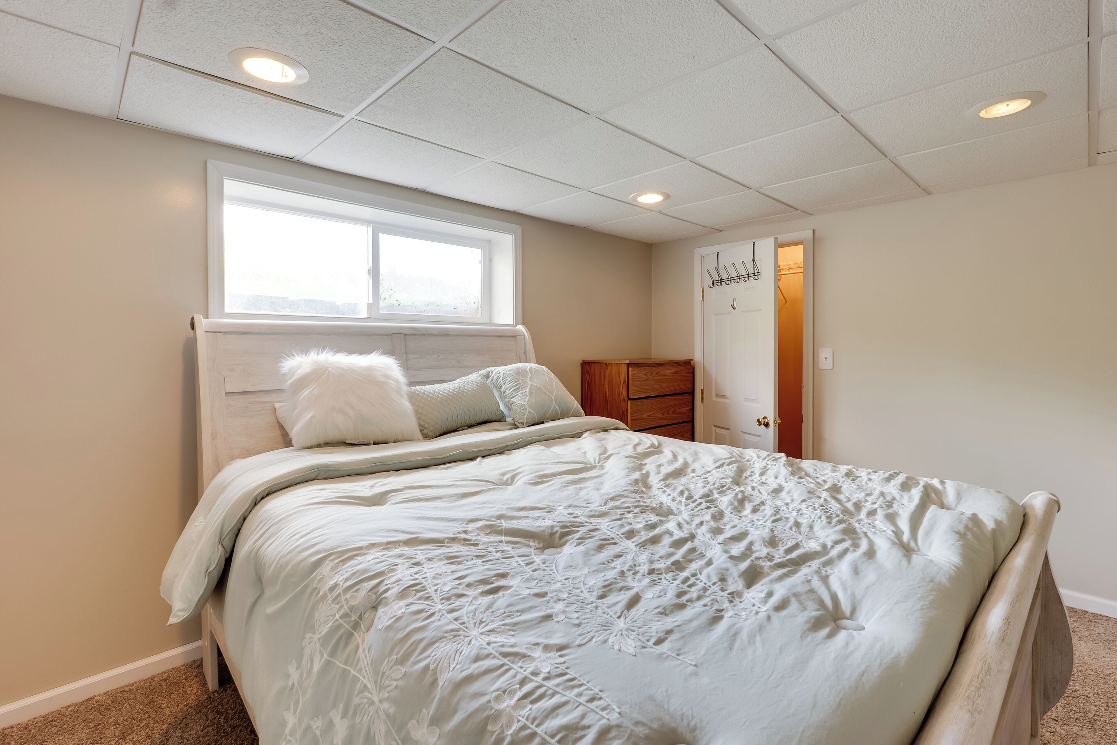Un dormitorio con cama, ventana, puerta e iluminación empotrada en el techo.