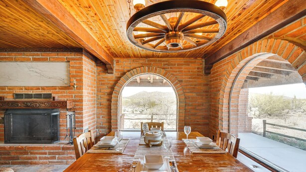 A dining area with a brick fireplace, wooden ceiling, and arched windows overlooking a landscape. - 10-acre Desert Oasis w/ Expansive Patio in Tucson! (Tucson)