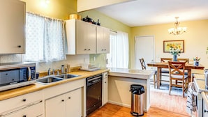 Une cuisine compacte avec des meubles blancs, un four à micro-ondes, un lave-vaisselle et un coin repas comprenant une table et des chaises en bois.